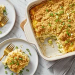 Baked and ready-to-serve million dollar chicken casserole in a white dish with a golden Ritz cracker topping, garnished with fresh green onions. Served with individual portions on plates, showcasing the creamy and cheesy layers of shredded chicken, cream cheese, and sour cream